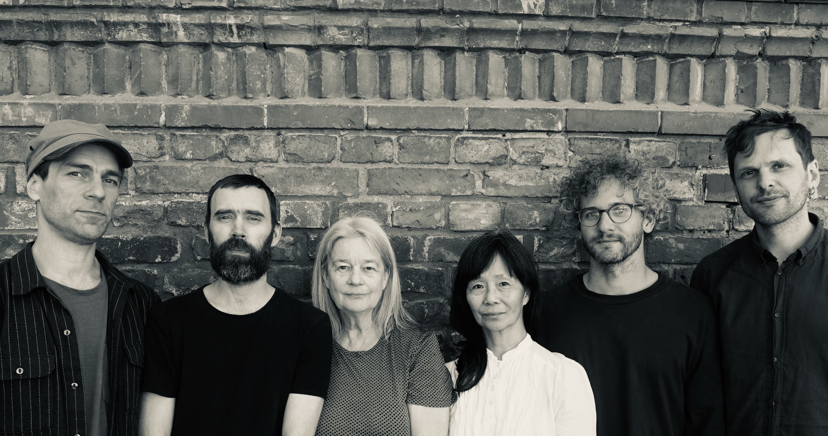 Six people standing in front of a brick wall, posing for a group photo.
